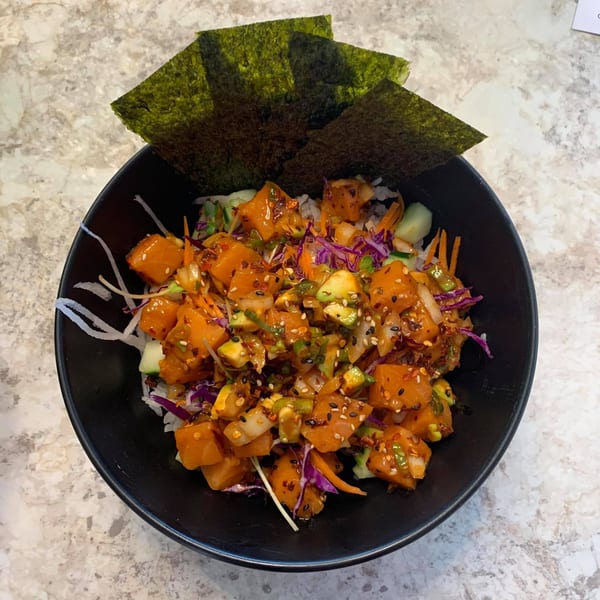 A Wabi Sabi poke bowl with salmon, avocado, and vegetables, topped with nori and sesame seeds.