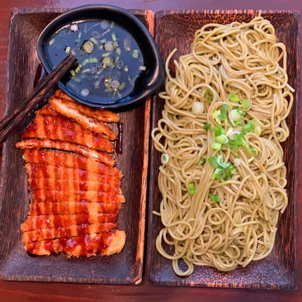 Japanese fried chicken with sauce and noodles, served on two dark wooden plates.