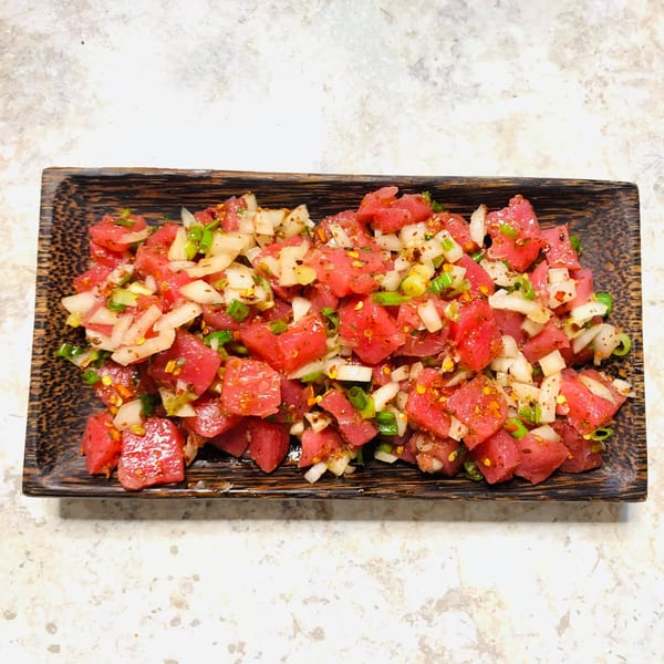 Wabi Sabi's fresh tuna poke with diced onions and green onions on a dark wooden plate.