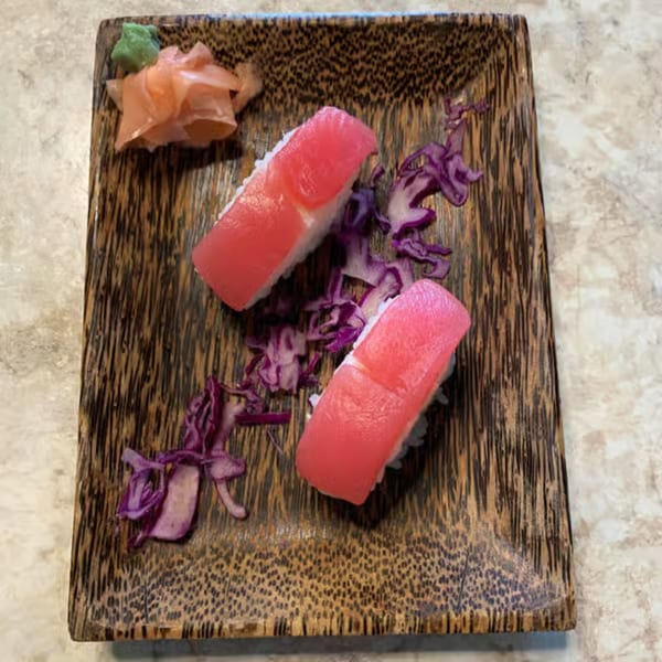 Two pieces of tuna nigiri sushi with pickled ginger, wasabi, and purple cabbage on a wooden plate.