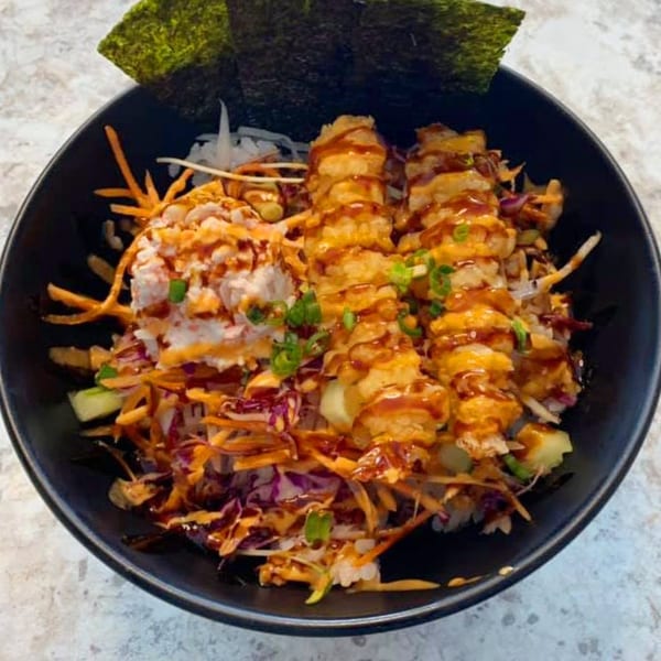 A Wabi Sabi Japanese dish with crispy shrimp, crab salad, colorful vegetables, and sauce in a black bowl.
