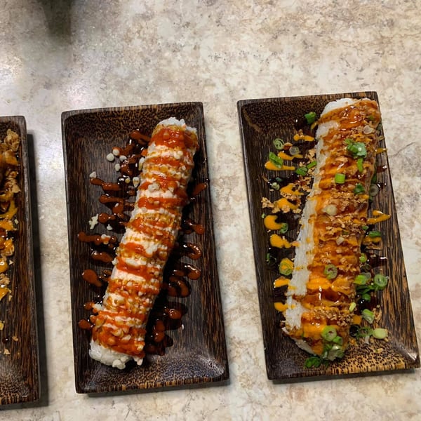 Two long sushi rolls, one with red sauce and the other with orange sauce and green onions.