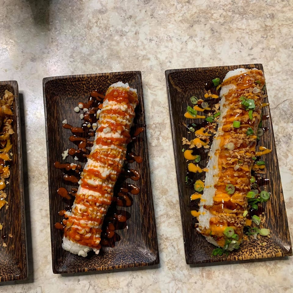 Two long sushi rolls, one with red sauce and the other with orange sauce and green onions.